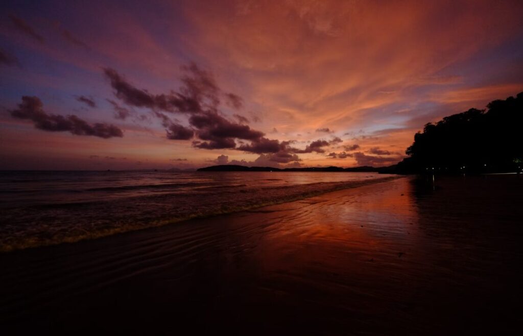 Malowniczy zachód słońca nad plażą Ao Nang w Tajlandii, z odbiciem barw na spokojnej wodzie.