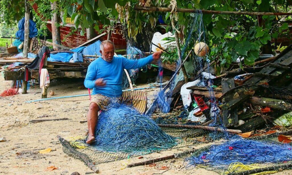 Tradycyjna wioska rybacka na Koh Mook, z lokalnymi mieszkańcami przygotowującymi łodzie na plaży.