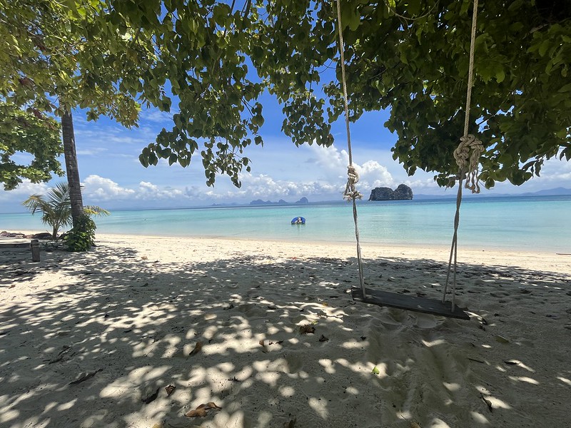 Drewniana huśtawka zawieszona na drzewie nad plażą Koh Ngai, z widokiem na turkusowe morze.