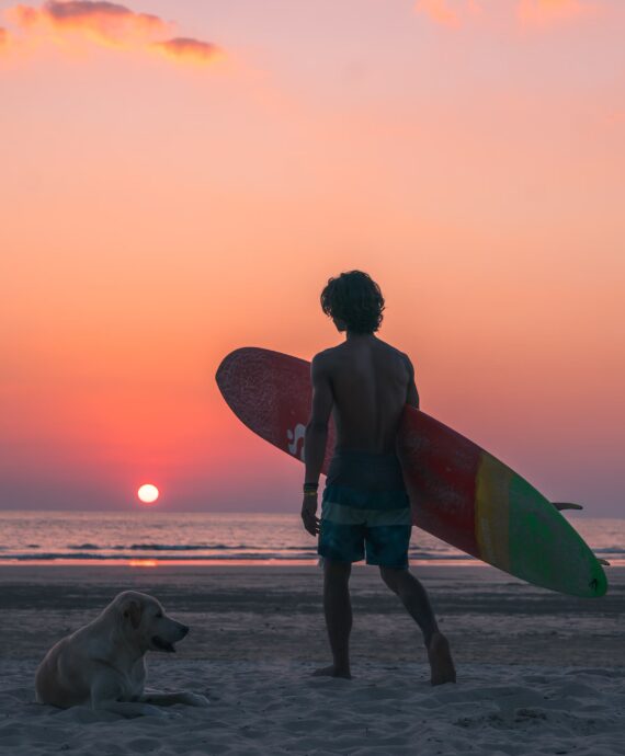 Surfer na plaży w Khao Lak o zachodzie słońca, trzymający deskę i patrzący na fale.