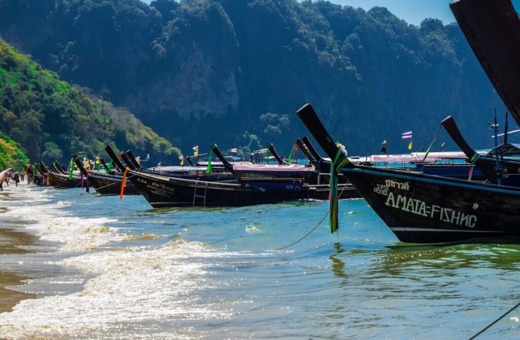 Tradycyjne tajskie łodzie longtail na wodzie w Ao Nang, Tajlandia, z malowniczymi wapiennymi klifami w tle.