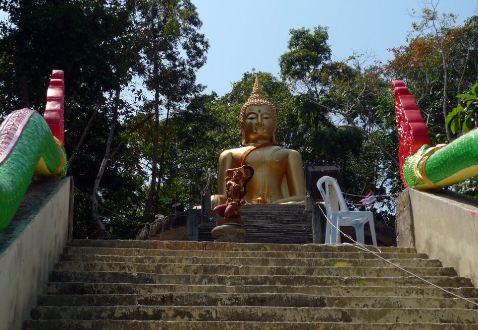 Świątynia na Koh Phayam otoczona tropikalną roślinnością, z posągiem Buddy i ozdobnymi schodami.