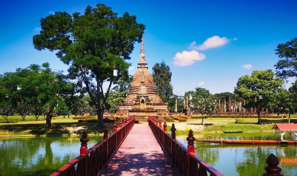 Świątynia Wat Sa Si w Sukhothai, położona na wyspie otoczonej wodą, z charakterystycznym posągiem Buddy i stupą w tle.