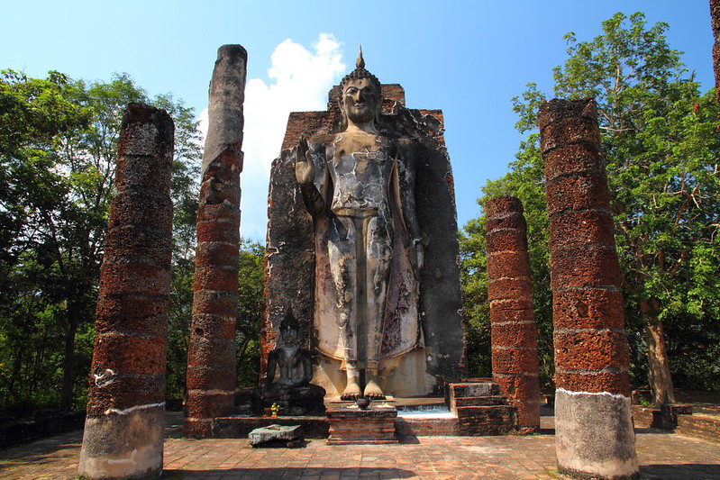 Ruiny świątyni Wat Saphan Hin w Sukhothai z wysokim posągiem stojącego Buddy otoczonym kamiennymi filarami.