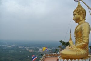 Złoty posąg Buddy na szczycie świątyni Tiger Cave Temple w Krabi, otoczony panoramicznym widokiem na dżunglę i Morze Andamańskie.