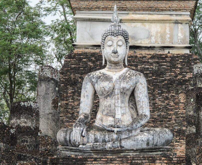 Ruiny świątyni Wat Traphang Ngoen w Sukhothai z dużym posągiem siedzącego Buddy na tle ceglanej ściany.