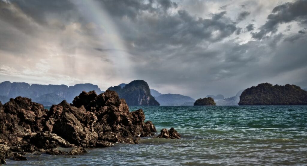 Widok na wyspę Koh Yao Noi z skalistym wybrzeżem i górami w tle, otoczony turkusową wodą Morza Andamańskiego.