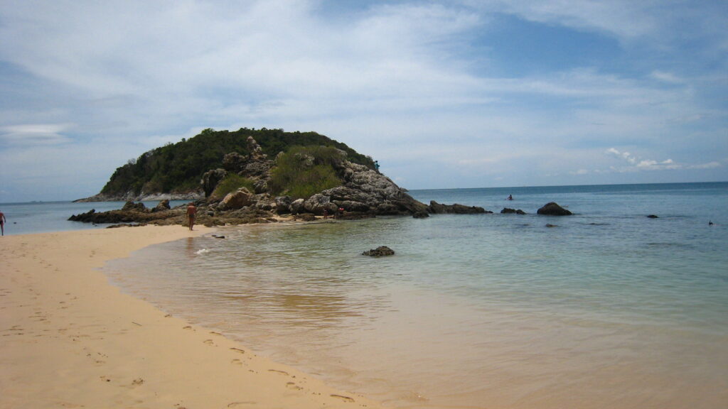 Spokojna plaża Ya Nui na Phuket – widok na piaszczyste wybrzeże z turkusową wodą i skałą w tle, o zachodzie słońca.