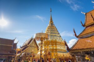Złota stupa świątyni Wat Phra That Doi Suthep w Chiang Mai, lśniąca w promieniach słońca na tle błękitnego nieba.