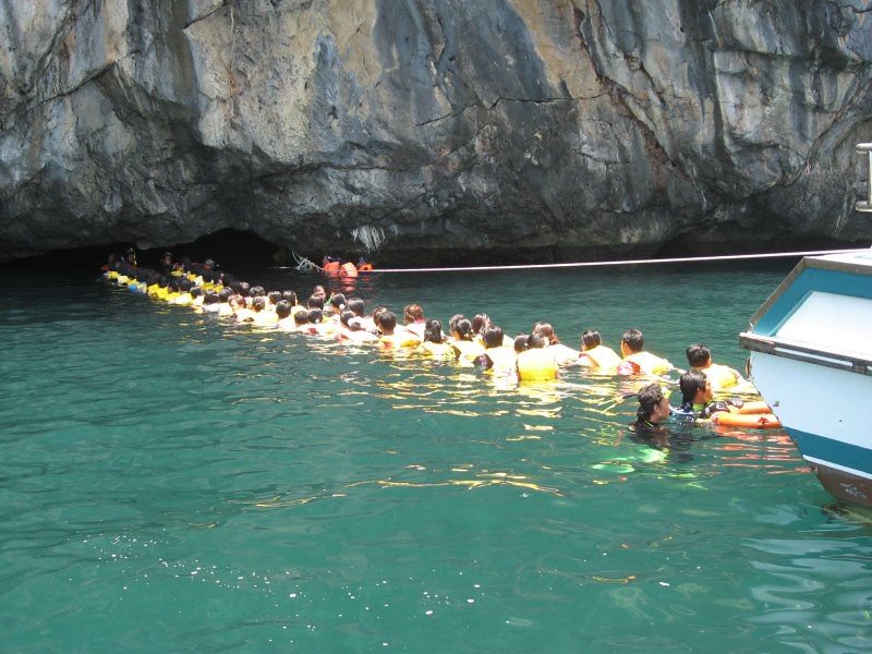 Grupa turystów wpływa do Szmaragdowej Jaskini (Emerald Cave) na Koh Mook, płynąc przez wąski tunel wodny.