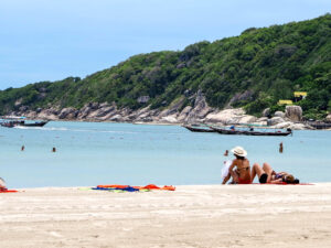 Widok na plażę Haad Rin na Koh Phangan z białym piaskiem, turkusową wodą i zielonymi wzgórzami w tle.