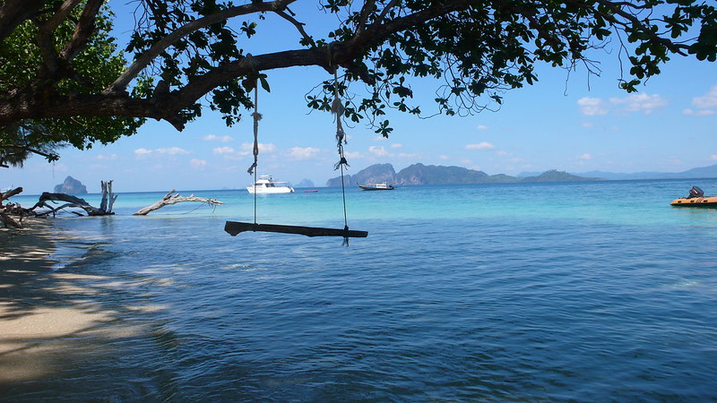 Drewniana huśtawka na plaży Koh Kradan, zawieszona na gałęzi drzewa, z widokiem na turkusowe morze.
