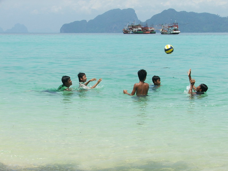 Plaża na Koh Kradan z dziećmi kąpiącymi się w turkusowej wodzie, w tle widoczne wyspy.