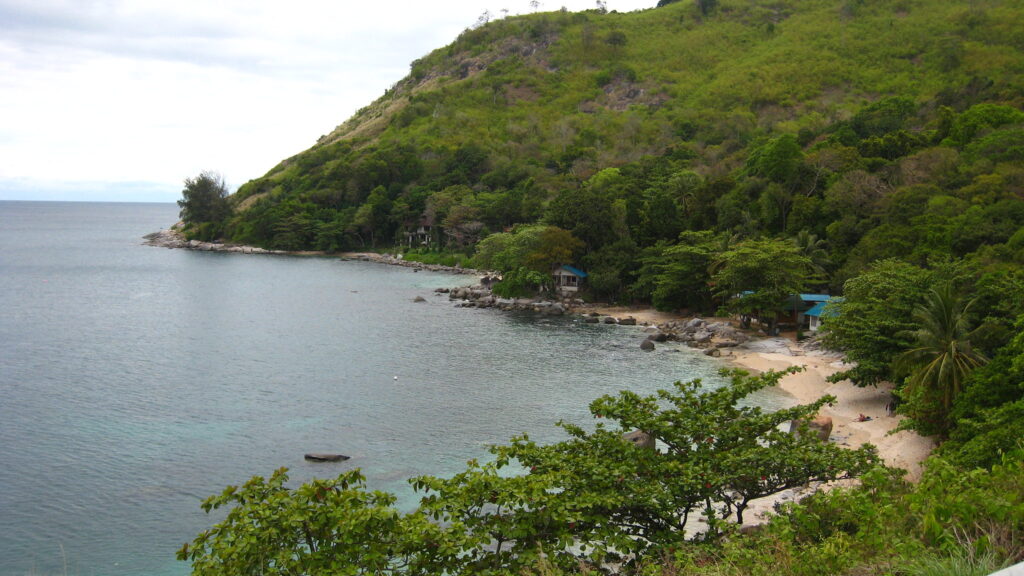 Widok na plażę Ao Sane na Phuket – niewielka zatoczka z kamienistym brzegiem i spokojnym morzem otoczona zielenią.