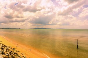 Szeroka, spokojna plaża Jomtien Beach w Pattaya o zachodzie słońca, z palmami i łagodnymi falami.